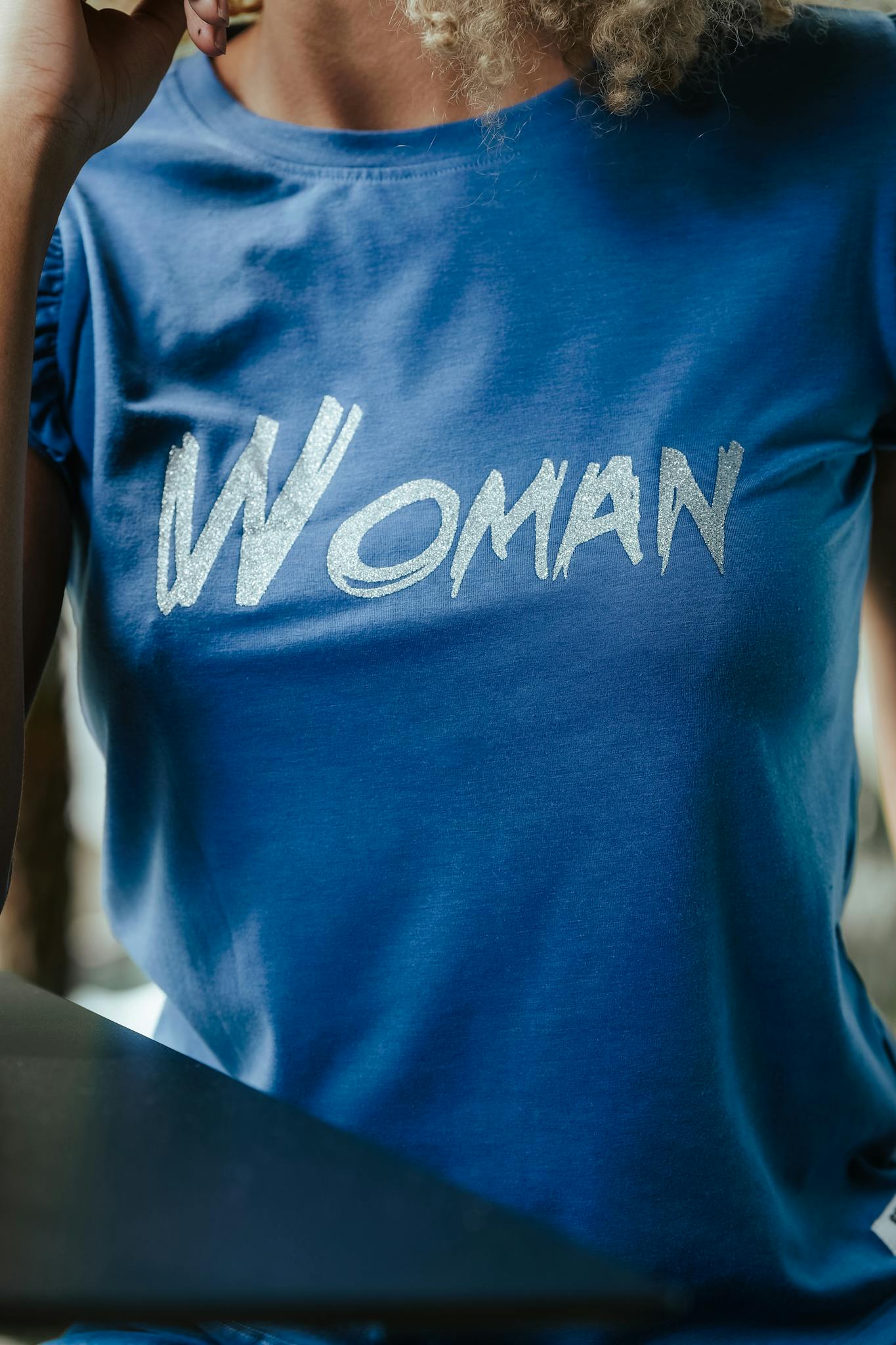 Close-up of a stylish blue t-shirt featuring bold 'Woman' text in a casual setting.